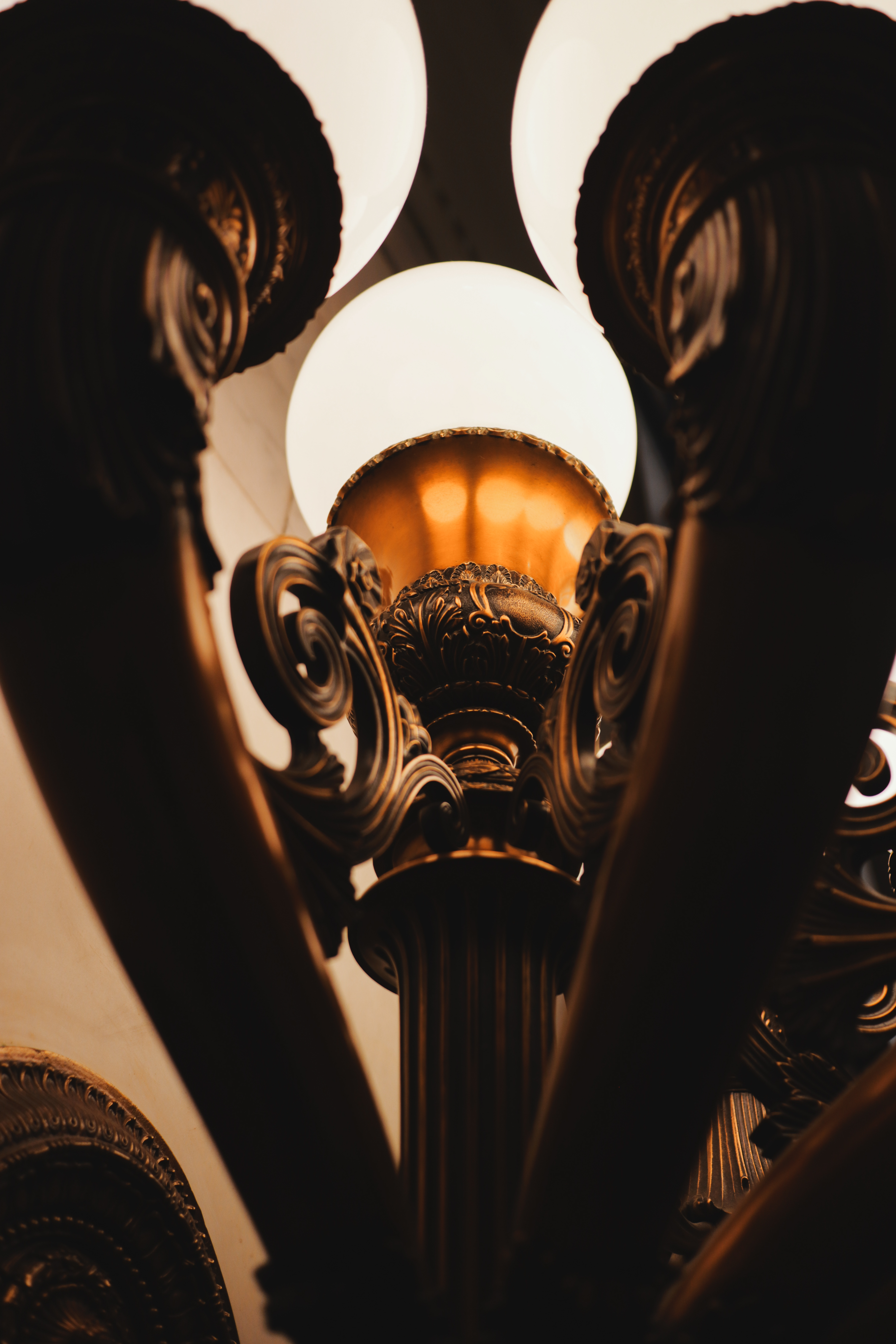 Ornate lamppost base looking up — warm bronze scrollwork, globe light above