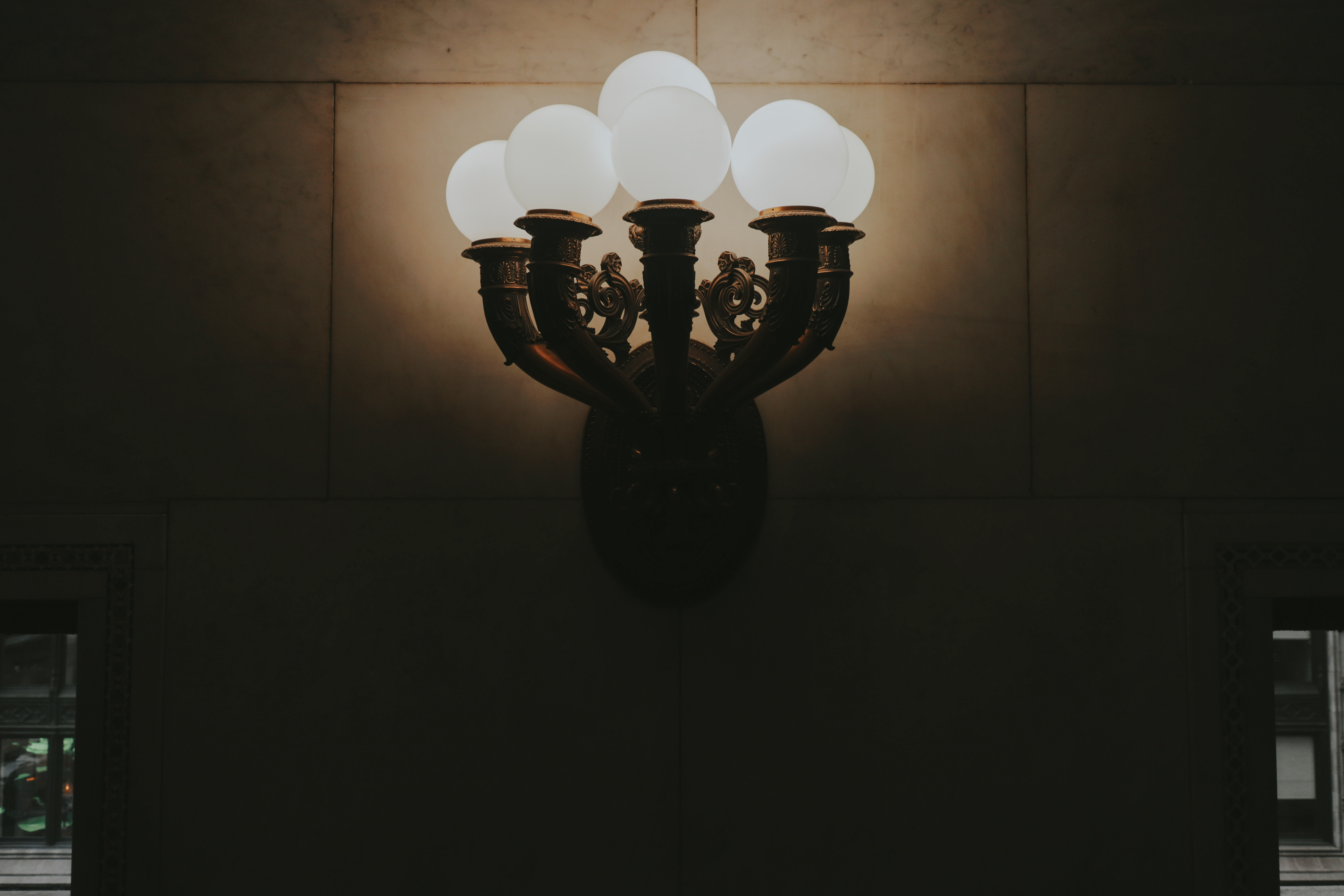 Five-globe ornate sconce mounted on dark marble wall — white globes glowing softly