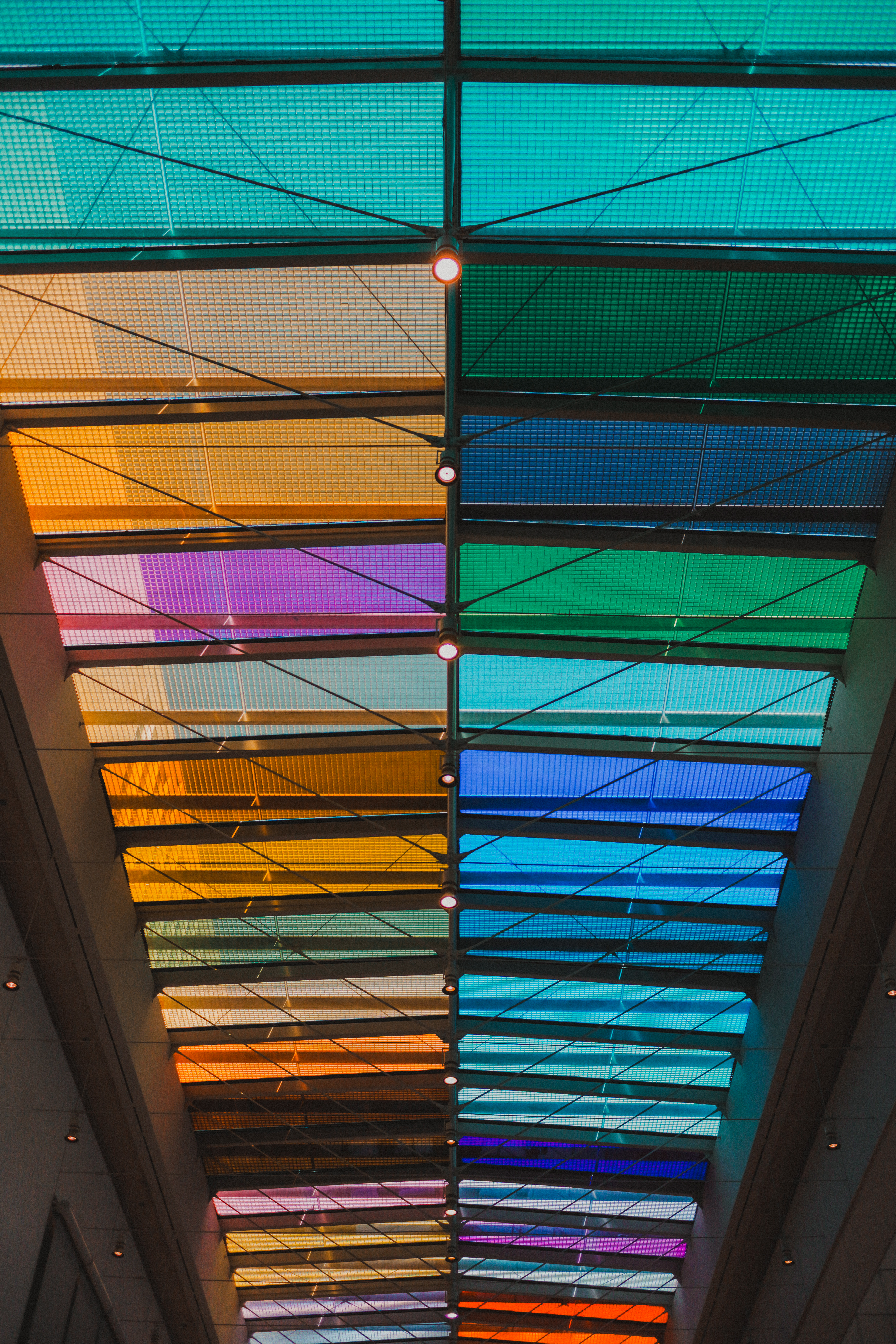 Rainbow glass ceiling panels — cyan, orange, purple, teal in grid across the Architecture Gallery