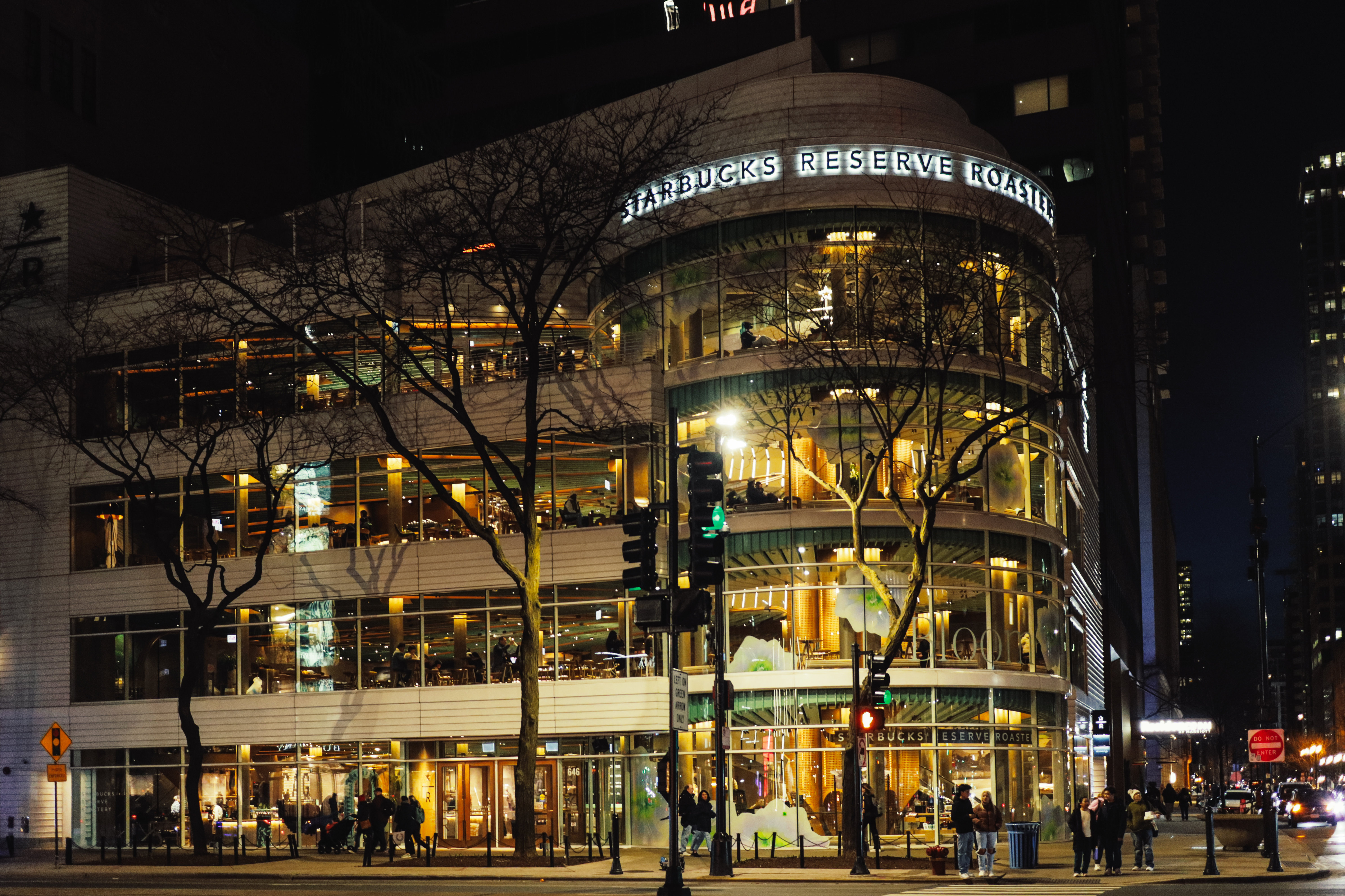 Starbucks Reserve Roastery exterior at night — warm golden glow through floor-to-ceiling glass