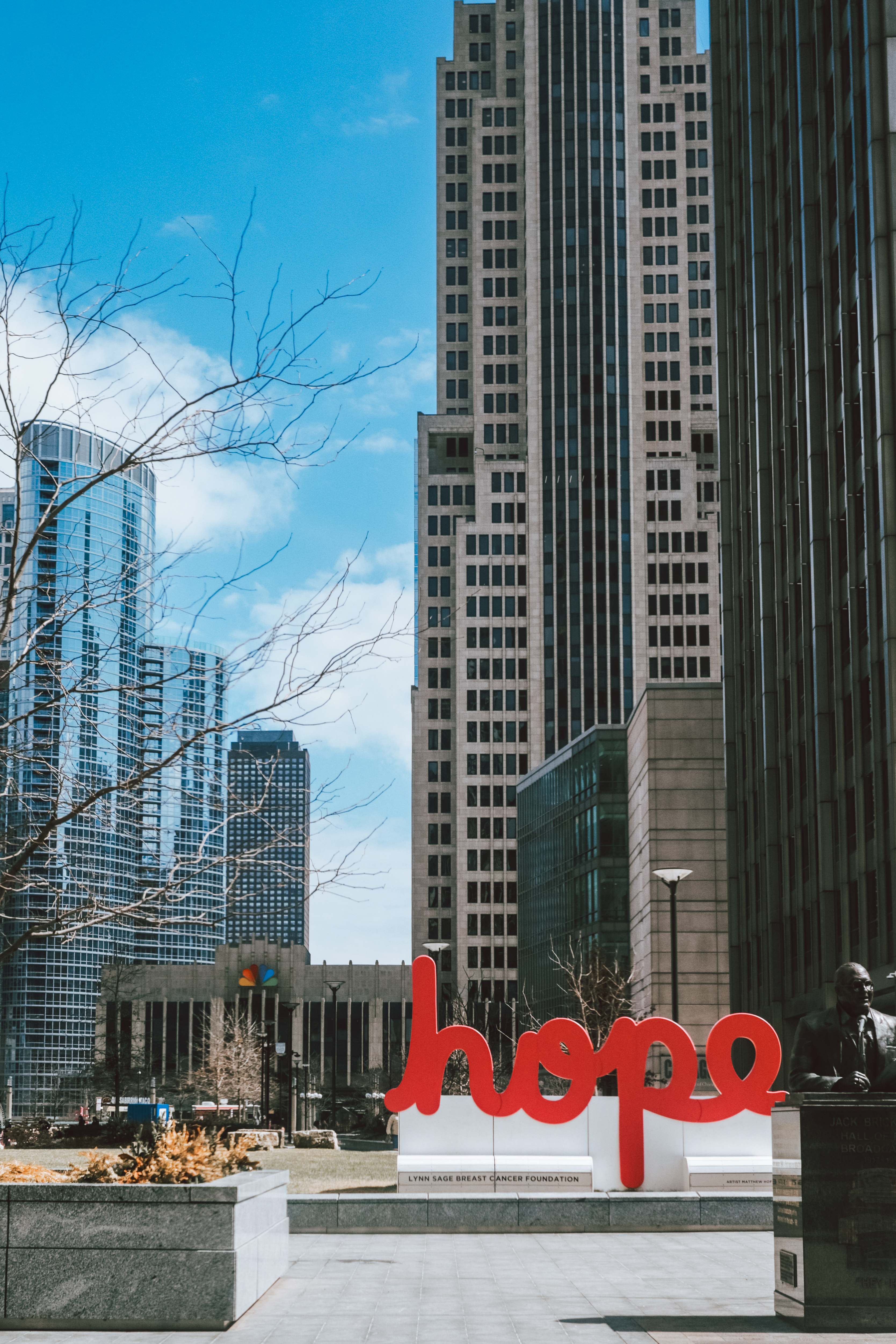 Red 'hope' sculpture in Wacker Drive plaza — skyscrapers rise behind bare winter trees