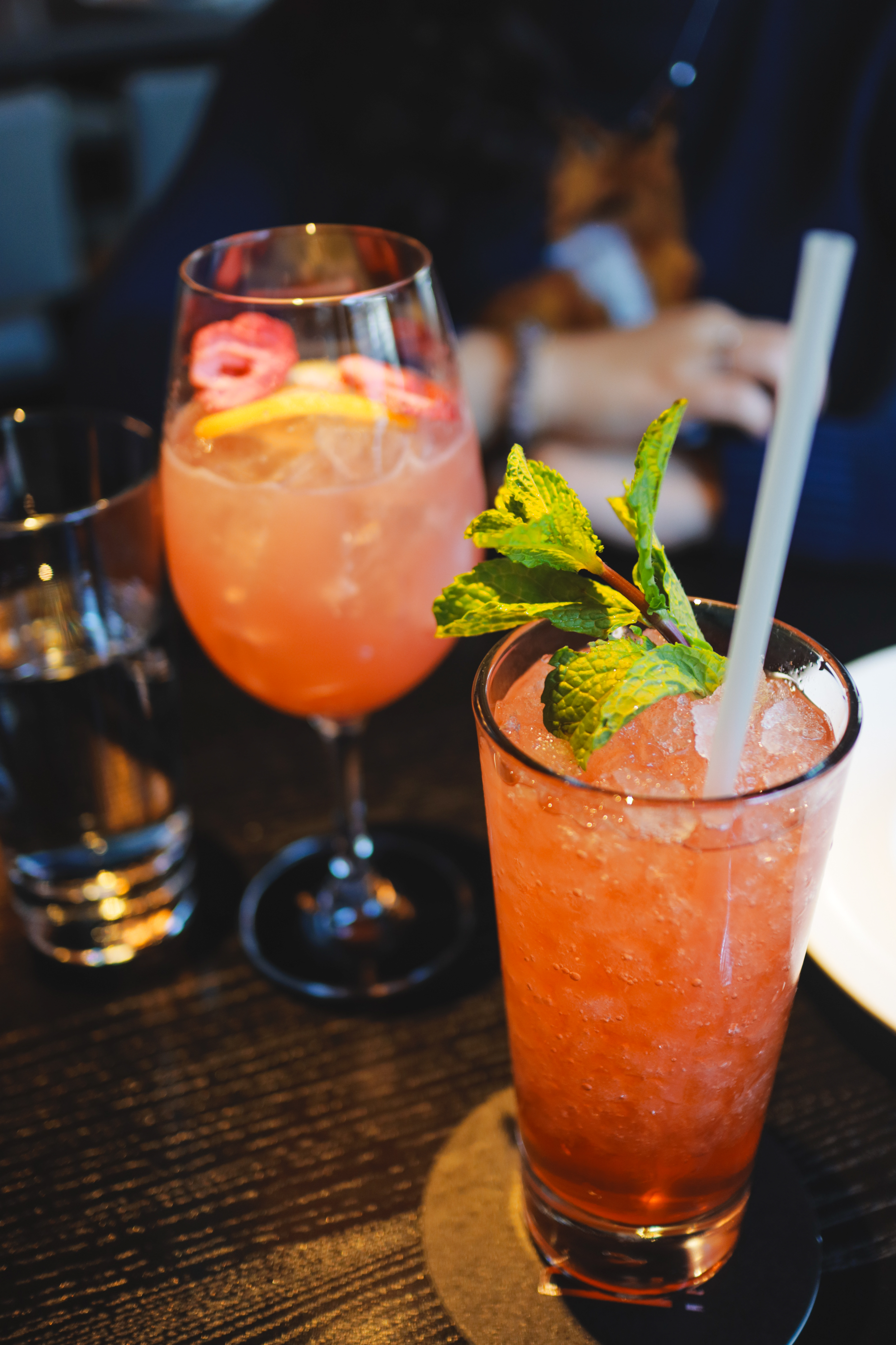 Two pink cocktails on dark bar table — spritz and highball with mint garnish
